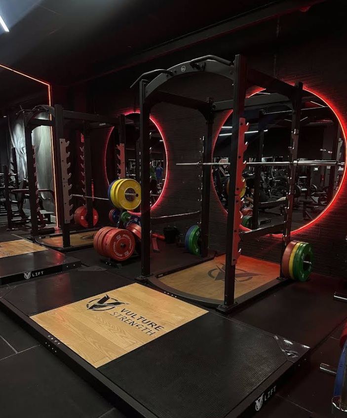 Zona funcional del gimnasio Vulture con espejos y neón magenta